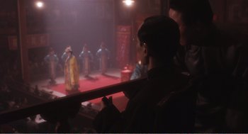 Movie still from “Farewell My Concubine” (1992), directed by Kaige Chen – A man in black jacket holding a cane in front of a group of people; Medium shot, Over the shoulder angle
