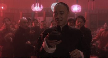 Movie still from “Farewell My Concubine” (1992), directed by Kaige Chen – A group of people gathered around a man holding a cup; Medium shot, Low angle