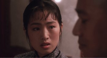 Movie still from “Farewell My Concubine” (1992), directed by Kaige Chen – A young asian woman looking at the camera with a man in the background; Close Up shot, Over the shoulder angle