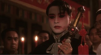 Movie still from “Farewell My Concubine” (1992), directed by Kaige Chen – A person with a mask holding a sword in front of candles; Close Up shot, Over the shoulder angle