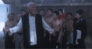 Movie still from “Farewell My Concubine” (1992), directed by Kaige Chen – An old man standing in front of a group of young men; Medium shot, Over the shoulder angle