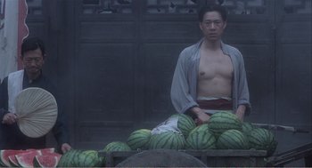 Movie still from “Farewell My Concubine” (1992), directed by Kaige Chen – A man sitting on top of a pile of watermelons; Medium shot, Low angle
