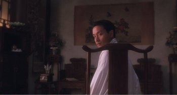 Movie still from “Farewell My Concubine” (1992), directed by Kaige Chen – A man sitting on a chair in a room; Medium shot, Over the shoulder angle