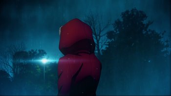 Movie still from “Fate/stay night [Heaven's Feel] I. presage flower” (2017), directed by Tomonori Sudô – A person wearing a red jacket standing in the rain at night; Extreme Wide shot, Low angle