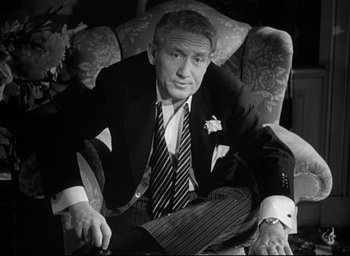 Movie still from “Father of the Bride” (1950), directed by Vincente Minnelli – An older man in a suit and tie sitting in a chair; Medium shot, High angle