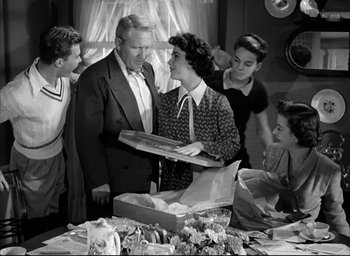Movie still from “Father of the Bride” (1950), directed by Vincente Minnelli – An old black and white photo of a woman holding a box; Medium shot, High angle