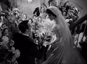 Movie still from “Father of the Bride” (1950), directed by Vincente Minnelli – A man and woman are holding hands in front of a group of people; Wide shot, High angle