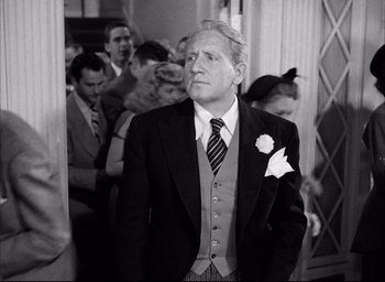 Movie still from “Father of the Bride” (1950), directed by Vincente Minnelli – An older man wearing a suit and tie in front of a group of people; Medium shot, Low angle