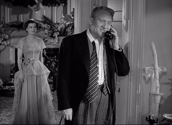 Movie still from “Father of the Bride” (1950), directed by Vincente Minnelli – An older man talking on a phone while a woman stands behind him; Medium shot, Low angle