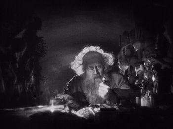 Movie still from “Faust” (1926), directed by F.W. Murnau – An old man sitting at a table smoking a pipe; Medium shot, High angle