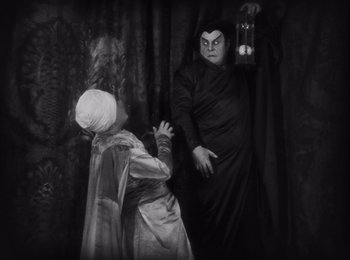 Movie still from “Faust” (1926), directed by F.W. Murnau – Two people dressed up in costumes in a dark room; Medium shot, High angle