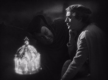 Movie still from “Faust” (1926), directed by F.W. Murnau – Two people are looking at a glass dome with lights inside it; Medium shot, High angle