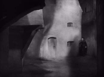 Movie still from “Faust” (1926), directed by F.W. Murnau – A black and white photo of a man standing in an alley; Extreme Wide shot, High angle