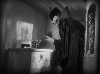 Movie still from “Faust” (1926), directed by F.W. Murnau – A man in a black robe holding something in his hand; Medium shot, High angle