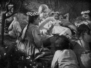 Movie still from “Faust” (1926), directed by F.W. Murnau – A group of people sitting in the grass with flowers in their hair; Medium shot, High angle