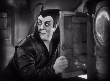 Movie still from “Faust” (1926), directed by F.W. Murnau – A man in a black jacket holding an open door; Medium shot, Over the shoulder angle