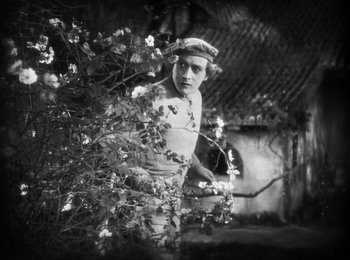 Movie still from “Faust” (1926), directed by F.W. Murnau – A man standing next to a bush with flowers in it; Medium shot, Over the shoulder angle
