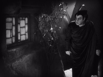 Movie still from “Faust” (1926), directed by F.W. Murnau – A person in a costume standing next to a tree; Medium shot, High angle