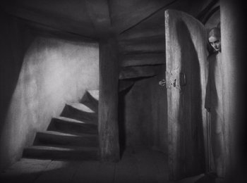 Movie still from “Faust” (1926), directed by F.W. Murnau – A black and white photo of a person standing in front of stairs; Wide shot, High angle
