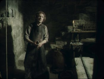 Movie still from “Faust” (2011), directed by Aleksandr Sokurov – A woman standing in a room holding a knife; Medium shot, High angle