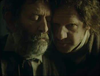 Movie still from “Faust” (2011), directed by Aleksandr Sokurov – A couple of men standing next to each other; Close Up shot, Over the shoulder angle