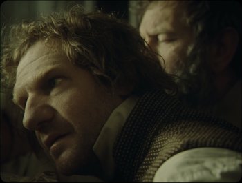 Movie still from “Faust” (2011), directed by Aleksandr Sokurov – A man with long hair and a beard is leaning on another man's shoulder; Close Up shot, Over the shoulder angle