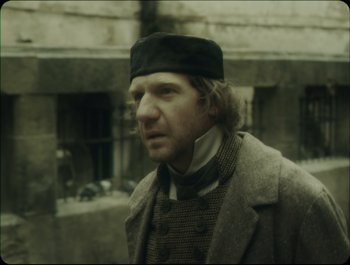 Movie still from “Faust” (2011), directed by Aleksandr Sokurov – A man wearing a black hat and a coat; Close Up shot, Over the shoulder angle