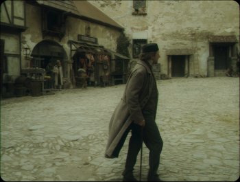 Movie still from “Faust” (2011), directed by Aleksandr Sokurov – An old man walking down the street with a coat on; Wide shot, Over the shoulder angle
