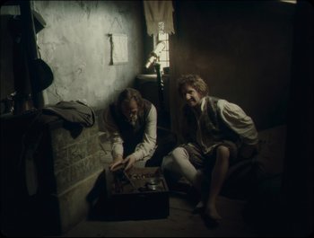 Movie still from “Faust” (2011), directed by Aleksandr Sokurov – Two men sitting on the floor in a room; Wide shot, High angle