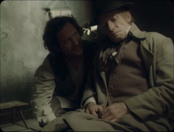 Movie still from “Faust” (2011), directed by Aleksandr Sokurov – A man sitting next to another man on a bed; Medium shot, Over the shoulder angle