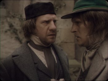 Movie still from “Faust” (2011), directed by Aleksandr Sokurov – Two men in suits and hats are standing next to each other; Medium shot, Over the shoulder angle