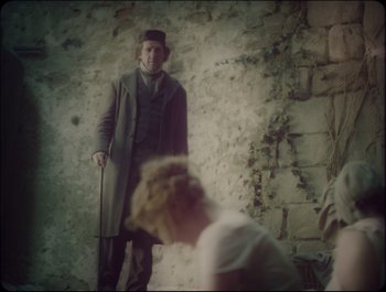 Movie still from “Faust” (2011), directed by Aleksandr Sokurov – A man standing in front of a stone wall; Medium shot, Over the shoulder angle