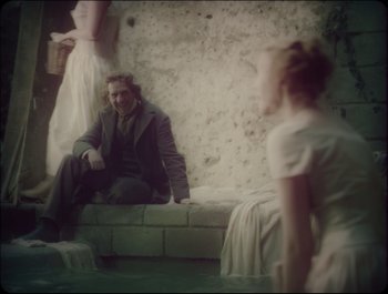 Movie still from “Faust” (2011), directed by Aleksandr Sokurov – A man sitting on a brick wall next to two women; Medium shot, Over the shoulder angle