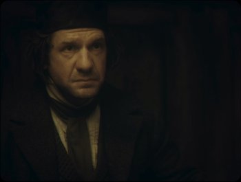 Movie still from “Faust” (2011), directed by Aleksandr Sokurov – A man in a hat and a jacket looking at the camera; Close Up shot, Over the shoulder angle