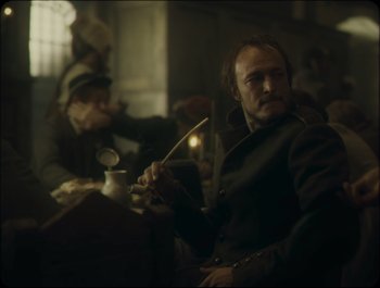 Movie still from “Faust” (2011), directed by Aleksandr Sokurov – A man sitting in a chair holding a knife in his hand; Medium shot, Over the shoulder angle