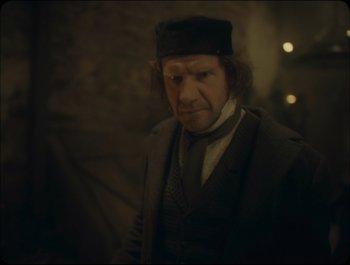 Movie still from “Faust” (2011), directed by Aleksandr Sokurov – A man wearing a hat and a suit; Close Up shot, Over the shoulder angle