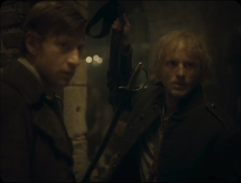 Movie still from “Faust” (2011), directed by Aleksandr Sokurov – Two men in trench coats are standing next to each other; Medium shot, Over the shoulder angle