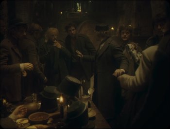 Movie still from “Faust” (2011), directed by Aleksandr Sokurov – A group of people standing around a table; Wide shot, High angle