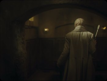 Movie still from “Faust” (2011), directed by Aleksandr Sokurov – An old man wearing a long coat walking through a tunnel; Wide shot, Over the shoulder angle