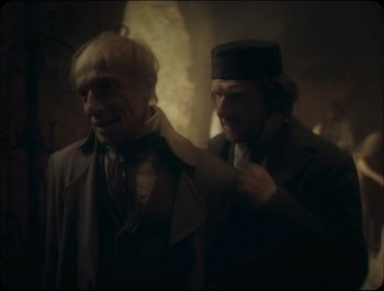 Movie still from “Faust” (2011), directed by Aleksandr Sokurov – Two men in suits and hats one of which is adjusting the tie of the other; Medium shot, Over the shoulder angle