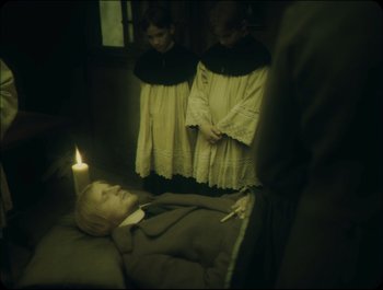 Movie still from “Faust” (2011), directed by Aleksandr Sokurov – Two little girls standing next to a doll with a lit candle; Medium shot, High angle