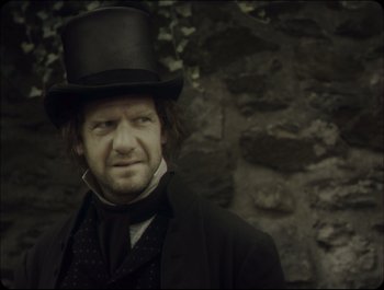 Movie still from “Faust” (2011), directed by Aleksandr Sokurov – A person wearing a top hat; Close Up shot, Over the shoulder angle