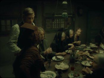Movie still from “Faust” (2011), directed by Aleksandr Sokurov – A group of people sitting at a table with plates of food on it; Wide shot, High angle