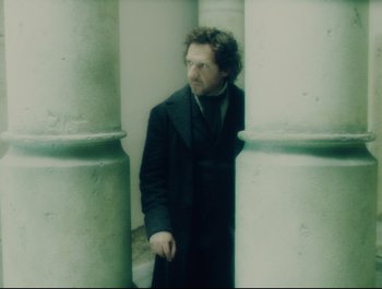 Movie still from “Faust” (2011), directed by Aleksandr Sokurov – A man in a black coat standing next to a pillar; Medium shot, Low angle