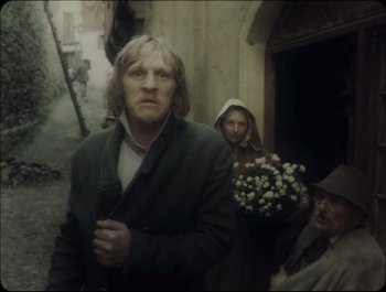 Movie still from “Faust” (2011), directed by Aleksandr Sokurov – A man standing next to a woman holding flowers; Medium shot, Low angle