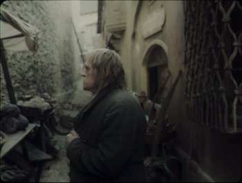 Movie still from “Faust” (2011), directed by Aleksandr Sokurov – A woman standing in an alleyway looking at something; Medium shot, Over the shoulder angle