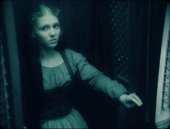 Movie still from “Faust” (2011), directed by Aleksandr Sokurov – A young girl sitting on a chair in a dark room; Medium shot, Low angle