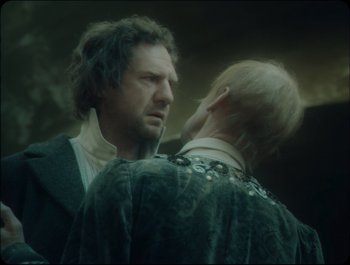 Movie still from “Faust” (2011), directed by Aleksandr Sokurov – Two men are facing each other in a dark room; Medium shot, Over the shoulder angle