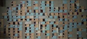 Movie still from “Fear X” (2003), directed by Nicolas Winding Refn – A wall covered in pictures of people with papers stuck to it; Extreme Close Up shot, High angle