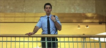 Movie still from “Fear X” (2003), directed by Nicolas Winding Refn – A man in a police uniform standing next to a railing; Medium shot, Low angle